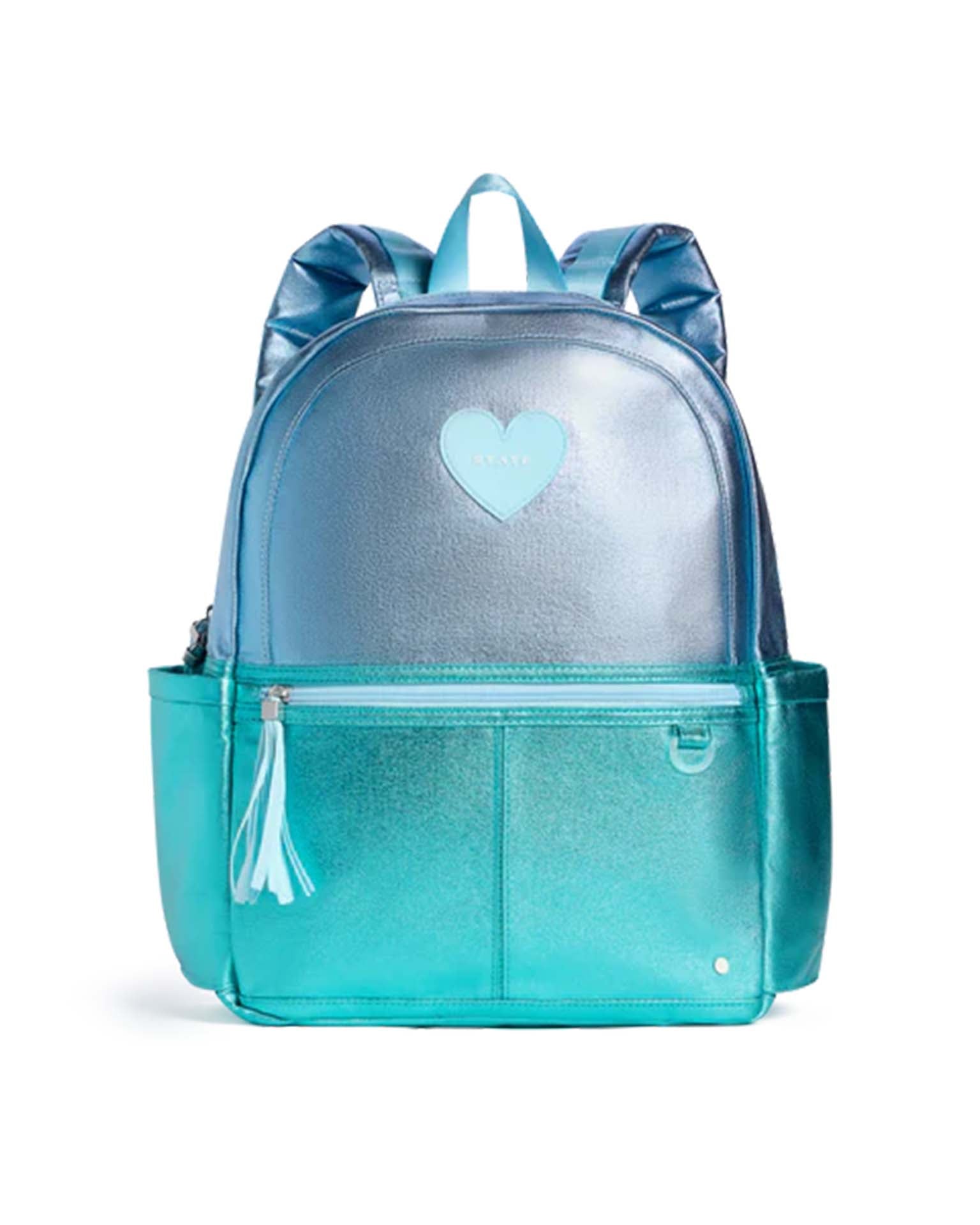 The STATE Bags Kane Backpack in blue and turquoise colorblock features a heart-shaped accent on the front pocket, tassel zipper pull, and convenient side pockets, shown against a white background.