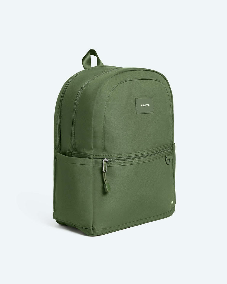 The Kane Large Double Pocket Backpack in Olive by State Bags stands upright against a plain light background, featuring a front zipper pocket, a side pocket, and a small STATE label on the front.