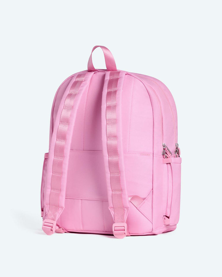 The kane large double pocket backpack in pink from state bags is shown from the back, highlighting its adjustable padded shoulder straps, top handle, and side pockets. The smooth surface and visible stitching details make this backpack an ideal choice for school or everyday use.