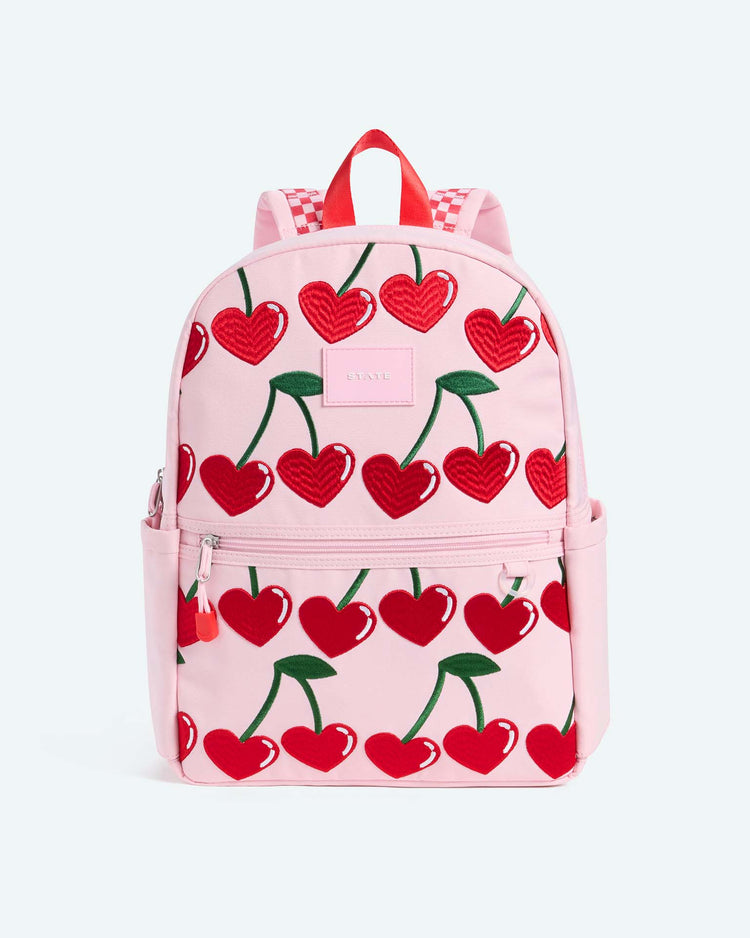 The kane backpack in cherry by state bags features a playful pink design with red heart-shaped cherries and green stems, along with convenient front and side pockets—perfect for everyday use and inspired by the signature style of state bags.