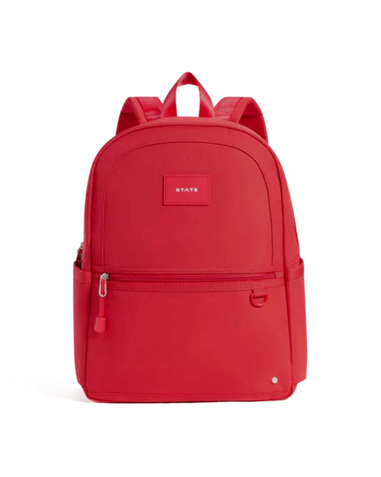 Introducing the Kane Backpack in Red by STATE Bags—a vibrant school backpack designed with a front zip pocket, convenient side pockets, and a sturdy top handle. This bag features two comfortable shoulder straps and is finished with a small rectangular STATE Bags label on the front, showcasing the brand’s renowned quality and style.