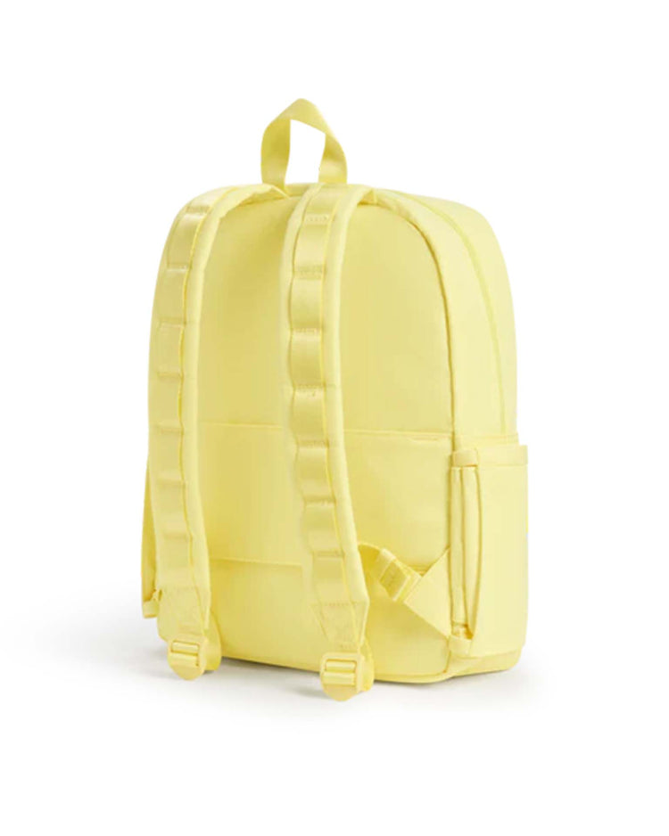 A butter yellow Kane backpack by State Bags, featuring padded shoulder straps and a top handle, is displayed from the back against a white background. The design is simple and minimal.