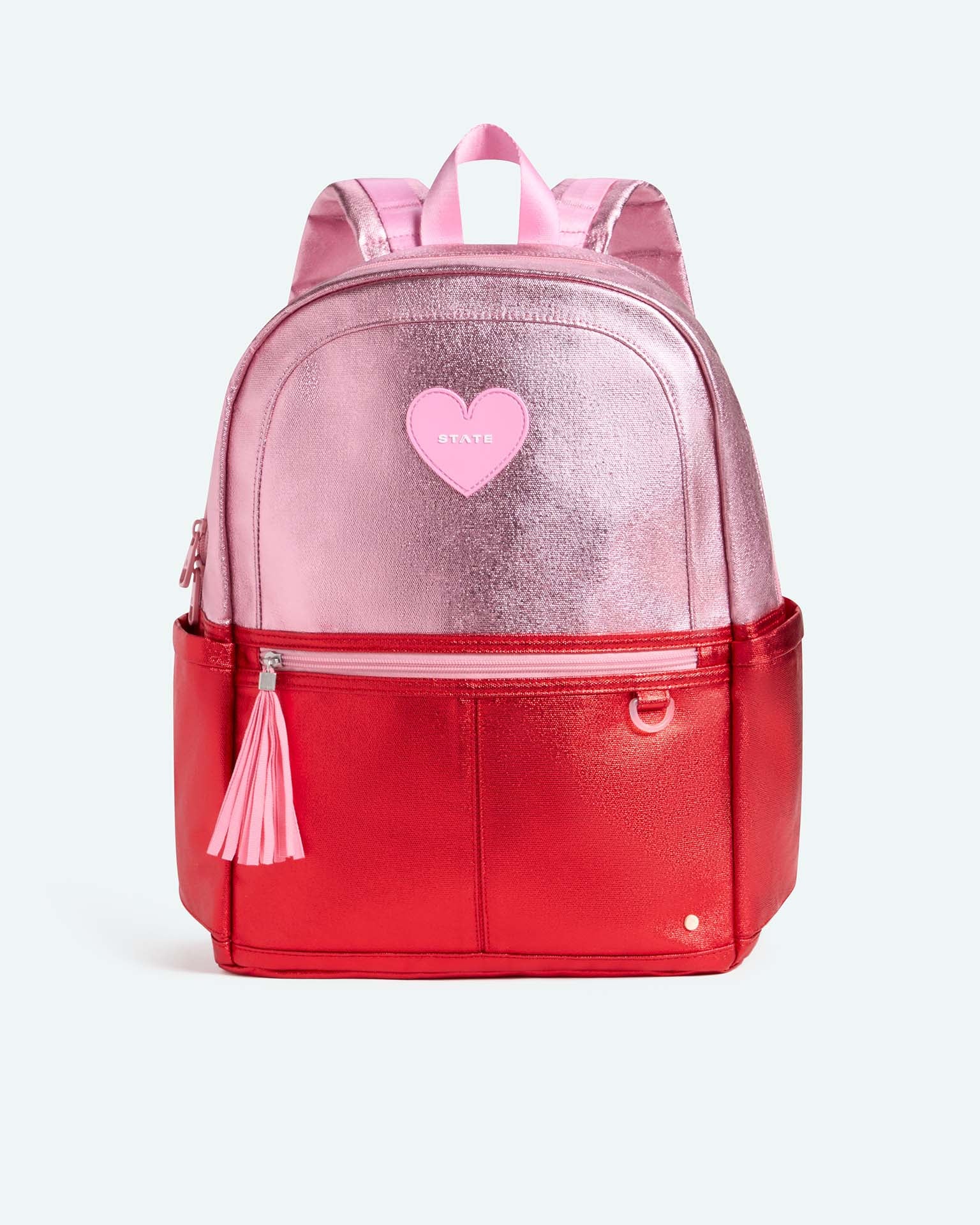 The Kane Large Double Pocket Backpack from State Bags features a striking pink and red colorblock design, complete with metallic pink on top, a bold red bottom, matching pink straps, a playful pink tassel, and a heart-shaped patch on the front that reads “STATE”—making it the perfect school backpack for anyone looking to make a statement.