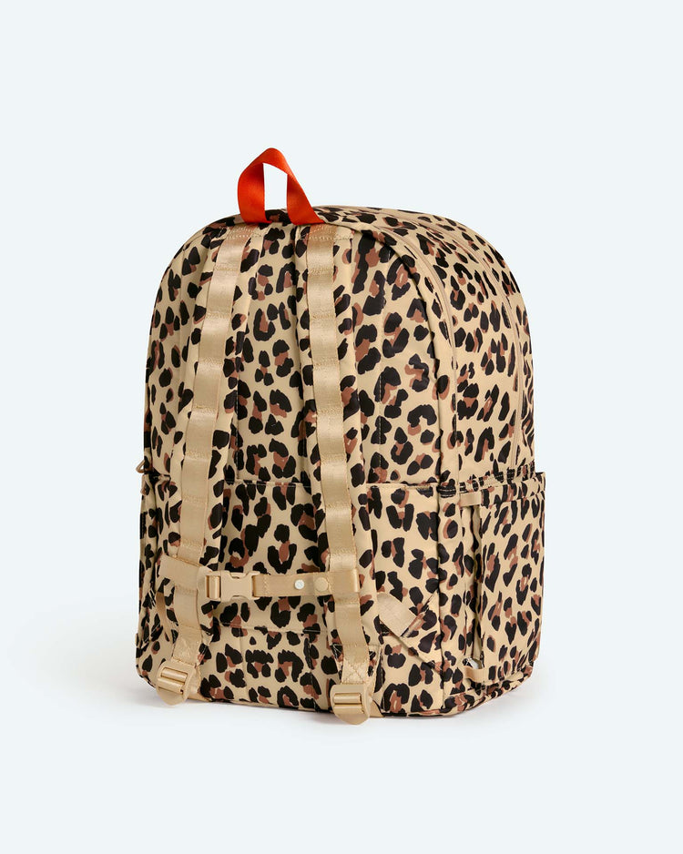 The reed backpack in leopard by state bags is showcased against a plain light background, featuring a brown and black leopard print, beige adjustable straps, side pockets, and a red carrying loop at the top. Designed for functionality and style for middle schoolers, this high-quality backpack also offers a padded laptop compartment for added protection.