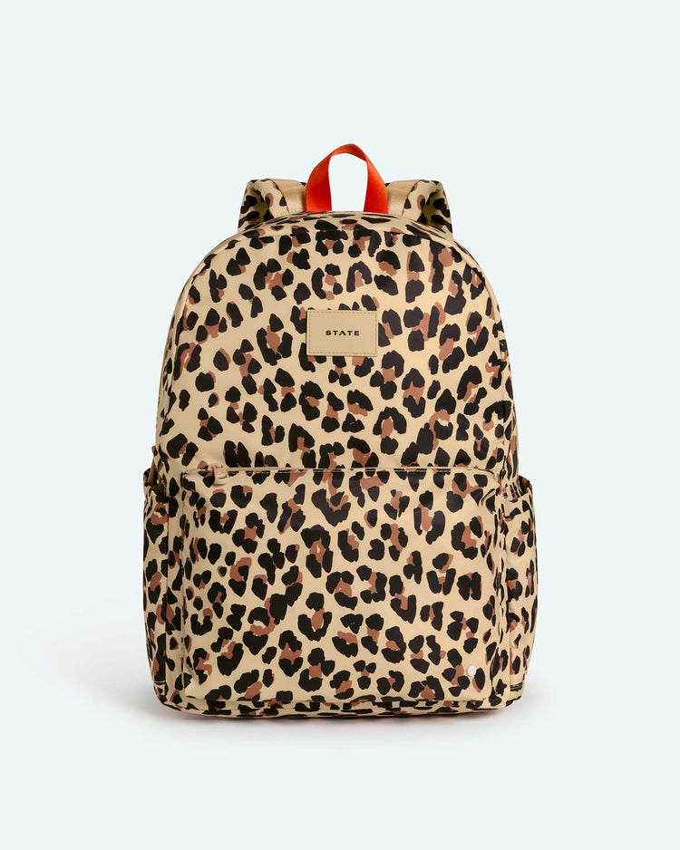 The reed backpack in leopard by state bags is a high-quality beige backpack with a brown and black leopard print pattern, featuring two side pockets, a front zipper pocket, an orange top handle, and a padded laptop compartment—perfect as a stylish middle school backpack.