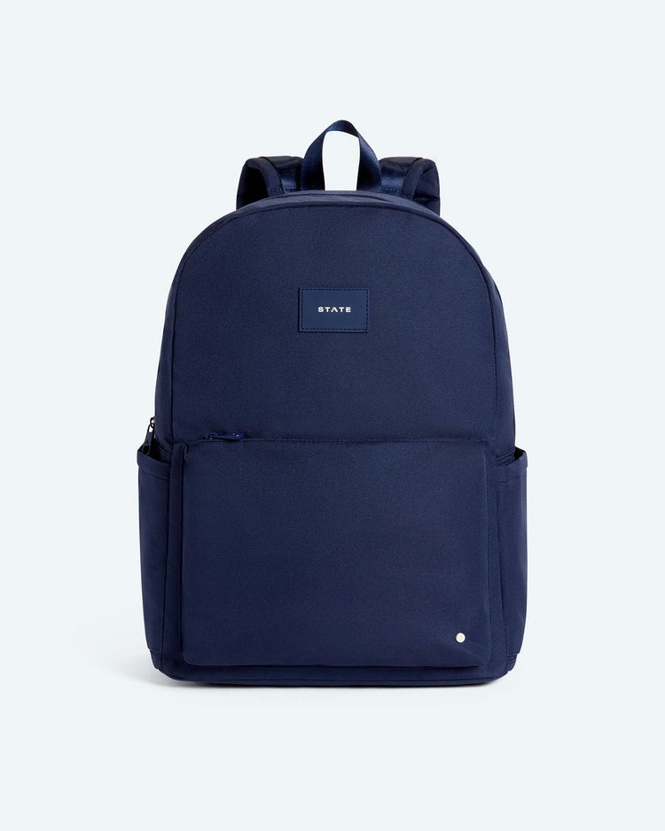 The reed backpack in midnight blue by state bags features a rectangular front pocket, two side pockets, and a small STATE patch on the front. Designed for middle schoolers, it offers padded shoulder straps, reinforced stitching for durability, and a simple, minimalist design.