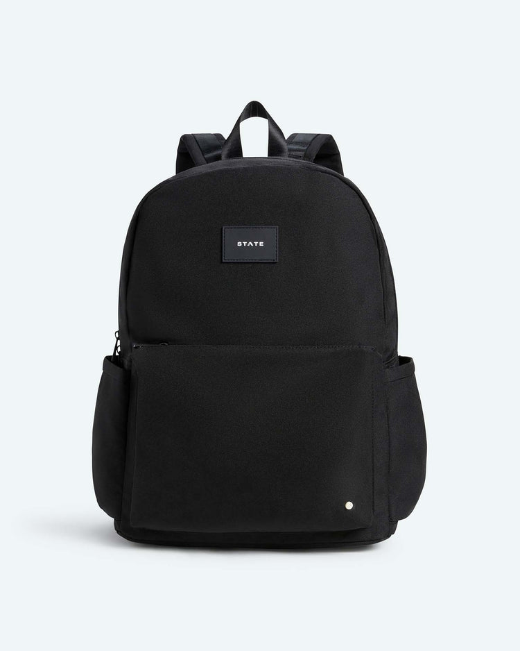 The Reed Backpack in Black by STATE Bags features a front pocket, side pockets, and a small rectangular label with the brand's name on the upper front. Designed for daily use as an ideal school backpack, it offers two comfortable shoulder straps and is displayed against a light gray background.
