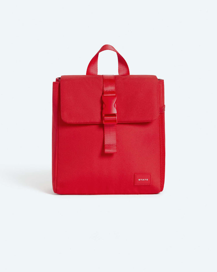 A bright red, square-shaped backpack with a top handle, front flap secured by a buckle, and a small rectangular logo patch at the bottom right—perfect for pairing with an insulated lunch bag or your child’s favorite STATE Bags richmond lunch sack in red.