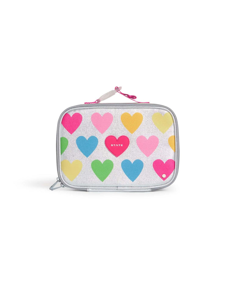 The State Bags Rodgers Lunch Box in Happy Fuzzy Hearts is a rectangular kids’ lunch box with a silver glittery surface, decorated with colorful heart shapes in pink, yellow, green, and blue. It features a top handle for easy carrying and a zipper closure.