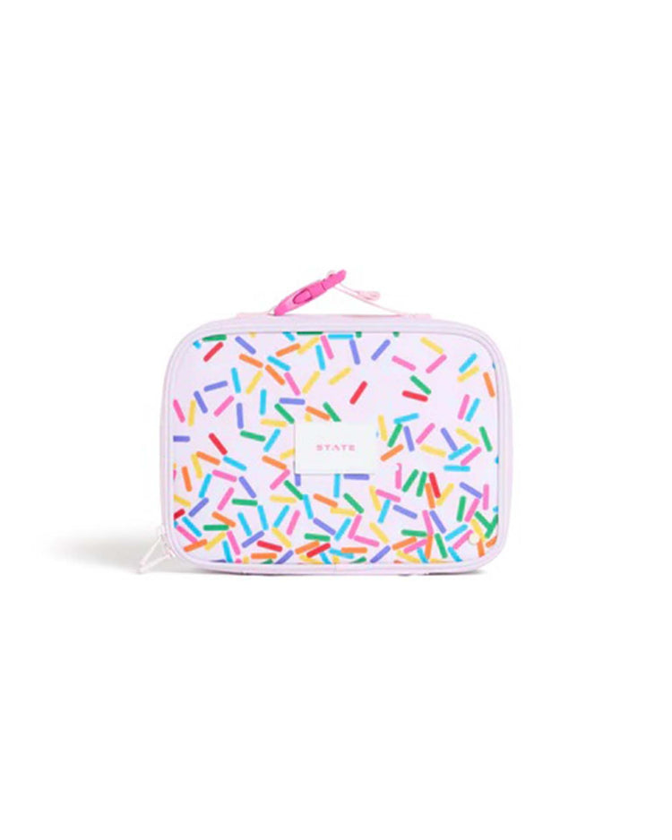 The Rodgers Lunch Box in Sprinkles by State Bags features a pastel pink design decorated with colorful sprinkles and a matching pink zipper. The STATE Bags logo is printed in the center, making this lunch box both stylish and practical for keeping meals fresh.