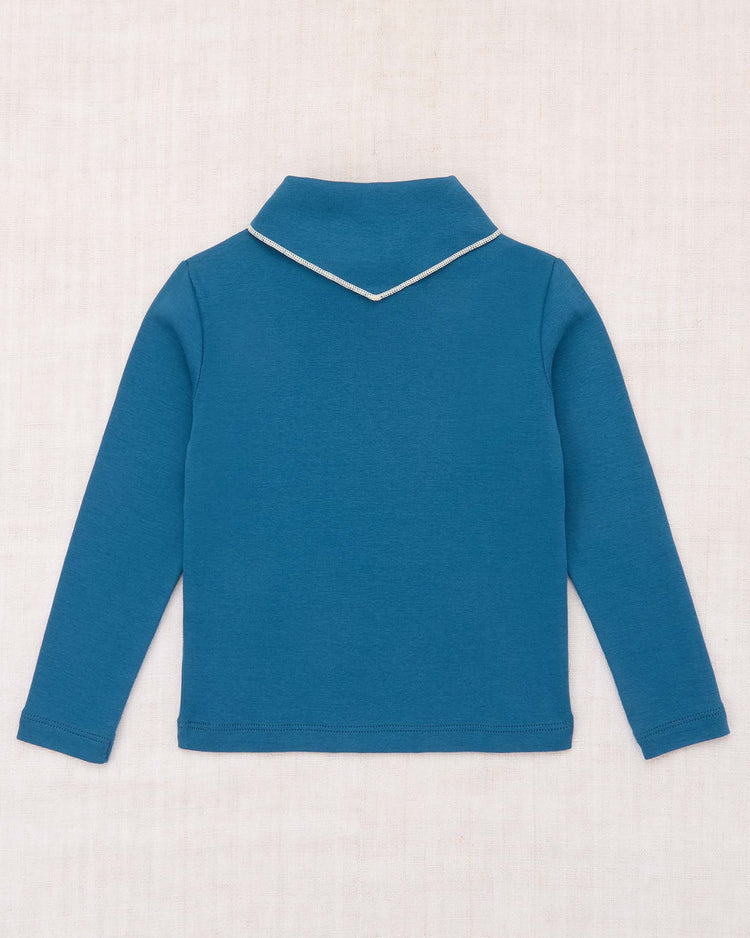 A long-sleeve scout top in blue smoke from misha + puff, featuring a collar and white trim, crafted from organic Pima cotton and shown laid flat on a light, textured surface with the back view displayed—an elevated signature piece.