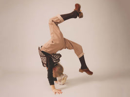 Kid dressed in Soor Ploom doing a handstand on a plain background