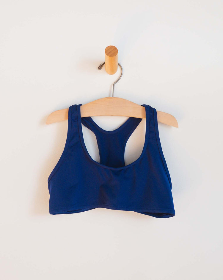 A sunchild luisa two-piece swimsuit in obscur, styled as girls swimwear, hangs on a wooden hanger from a wall hook against a plain white background.