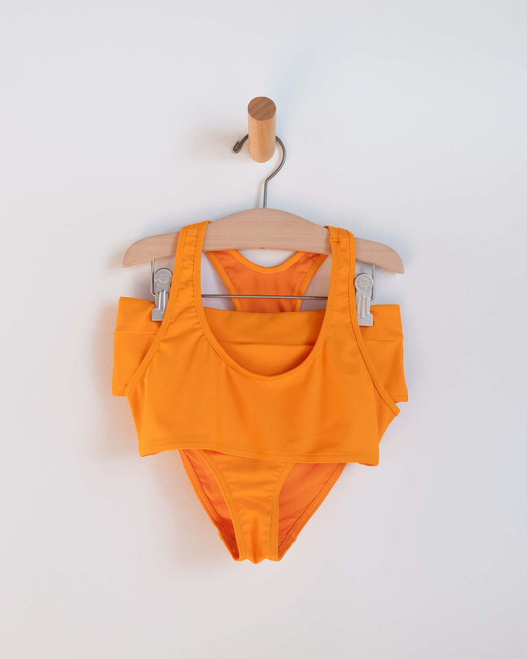 A luisa two-piece swimsuit in Inca by Sunchild, featuring a sleeveless top and high-waisted bottoms, hangs on a wooden hanger against a white background.