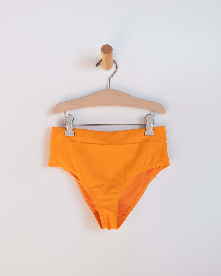 The luisa two-piece swimsuit in Inca by Sunchild features bright orange bikini bottoms clipped to a wooden hanger on a peg against a white background—an ideal pick for kids' swimwear and mix-and-match sets.