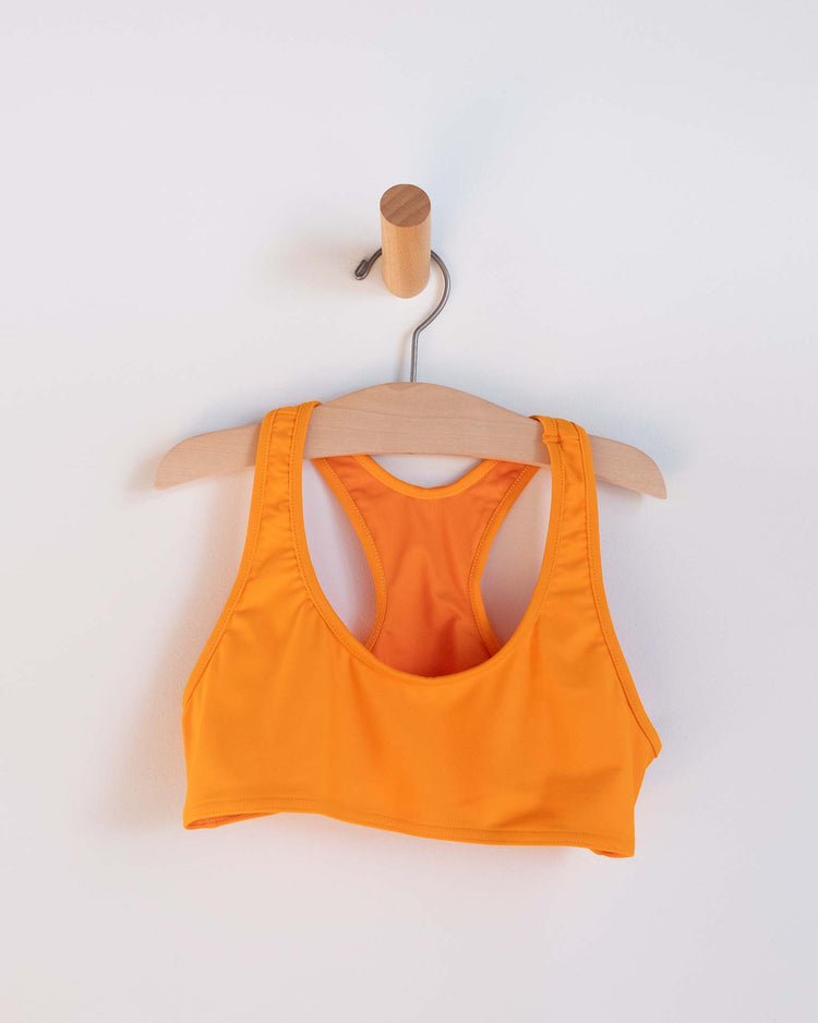 A vibrant orange luisa two-piece swimsuit in inca by Sunchild hangs on a wooden hanger hooked onto a simple wall peg against a plain white background.