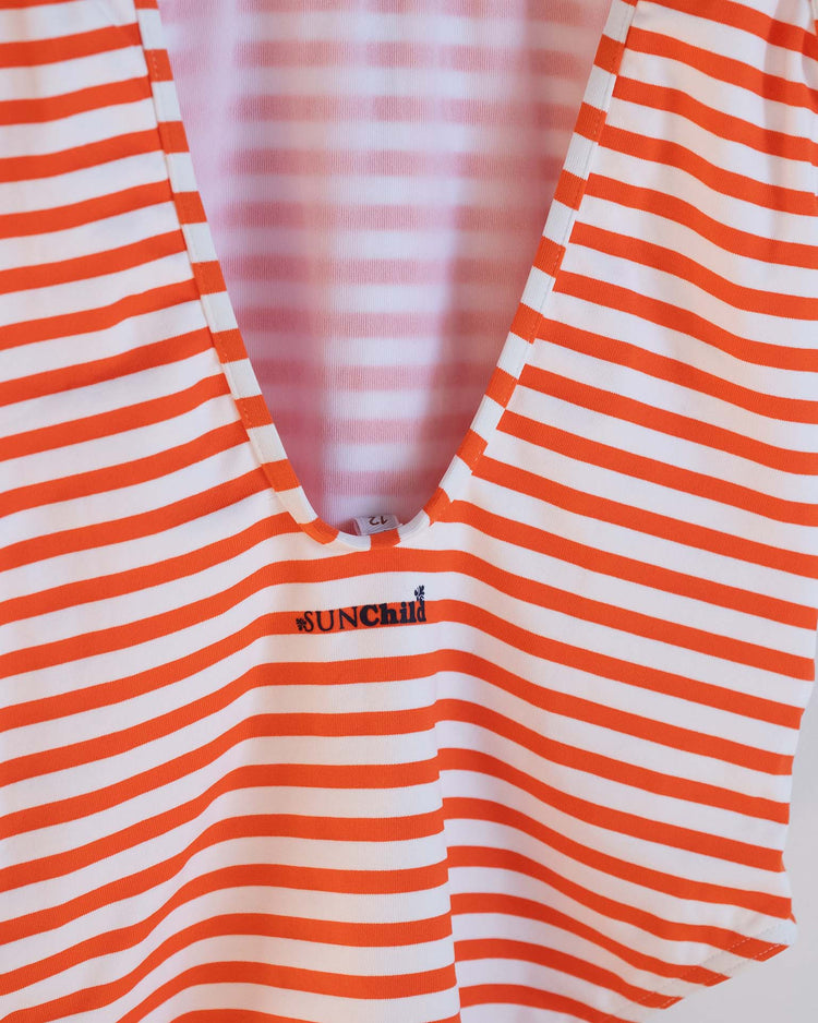 A close-up of the sunchild lou one-piece swimsuit in soda, featuring red and white stripes and a deep V neckline, with "sunchild" embroidered in black below the neckline, capturing relaxed summer swimwear vibes.