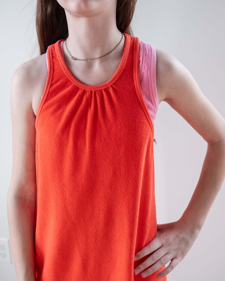 A person stands with one hand on their hip, wearing the Sunchild bilbao dress in tangerine. Their long brown hair falls down while their face is partially out of frame.