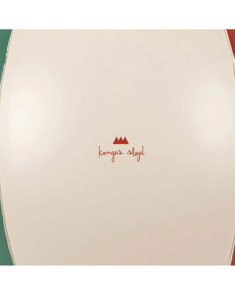 A close-up shows the cream-colored surface of the "beach ball in multi" by konges sløjd, featuring their centered red logo and text, with three small red triangles above—reflecting the design of their classic inflatable beach balls.