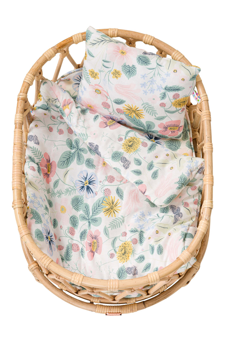 A beautifully handmade Poppie Crib Botanical Collection basket by poppie toys, featuring floral-patterned bedding and a matching pillow created by skilled craftsmen.