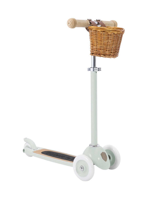 The banwood scooter in mint by Banwood is a light green three-wheel kick scooter with a tan handlebar, black footboard, white wheels, a brown wicker basket on the front, and features an Easy Ride Steering System for smooth control.