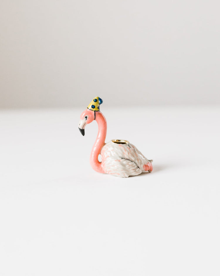 A small hand-painted ceramic flamingo cake topper with intricate detailing, positioned against a plain white background by Camp Hollow.