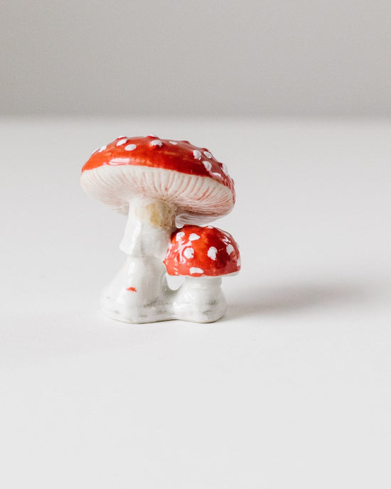 Two small ceramic Camp Hollow mushroom cake toppers, red with white spots, on a plain white background.