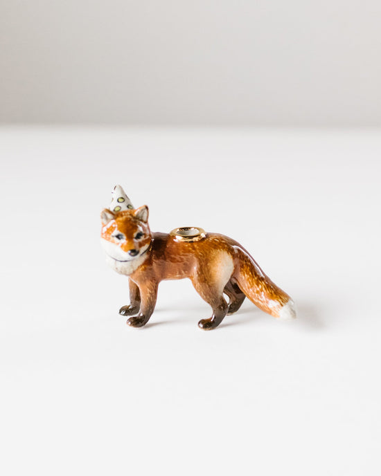 A hand-painted ceramic red fox cake topper from Camp Hollow, wearing a party hat and doubling as a ring holder, on a plain white background.