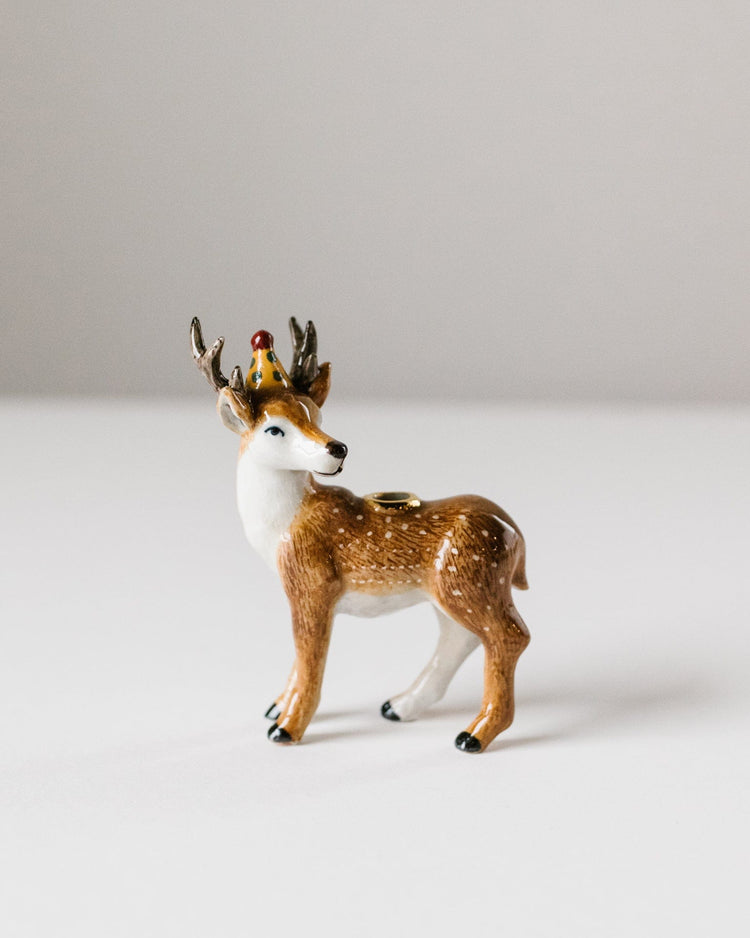 A small porcelain figurine of a Camp Hollow stag cake topper with a crown and heirloom-quality craftsmanship, standing against a plain, light background.