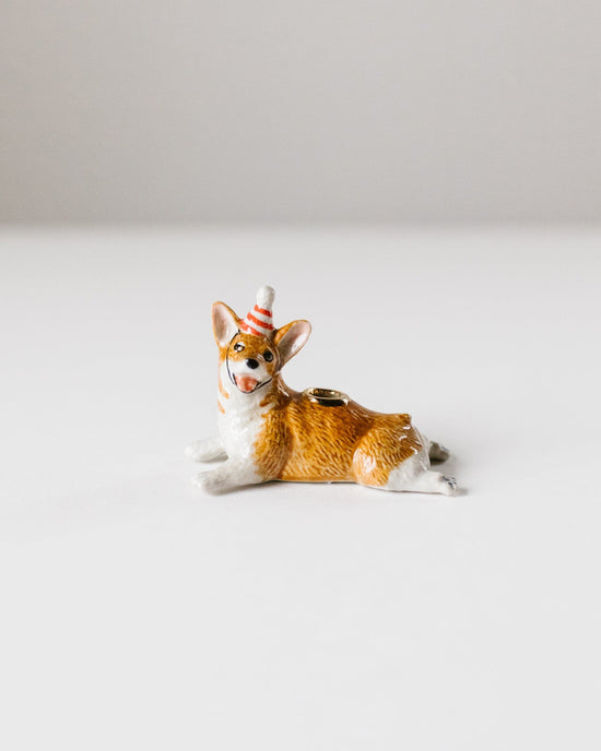 A hand-painted ceramic figurine of a lounging fox wearing a striped party hat, positioned on a plain white background by Camp Hollow's Year of the Dog cake topper.
