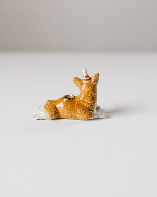 A small hand-painted figurine of a fox sitting on a snowy base, facing backward with a tiny red-and-white lighthouse on its back. This is the camp hollow year of the dog cake topper.
