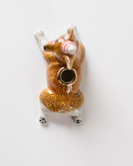 A small hand-painted figurine of a brown and white dog wearing a red and white striped hat and a black bell collar, positioned against a plain white background, from Camp Hollow's Year of the Dog cake topper collection.