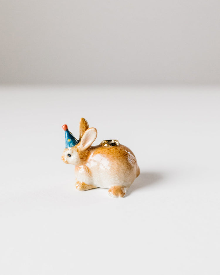A small hand-painted porcelain Year of the Rabbit cake topper with a blue party hat, set against a plain white background by Camp Hollow.