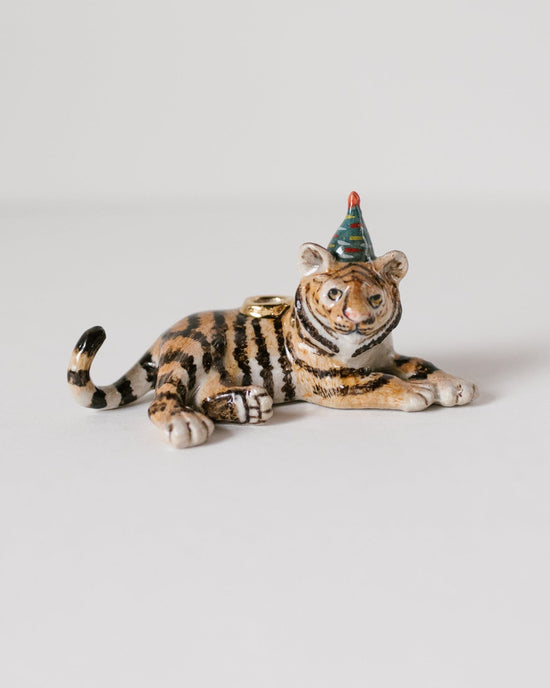 A Camp Hollow year of the tiger cake topper with a party hat, lying down and facing the camera, on a plain white background.