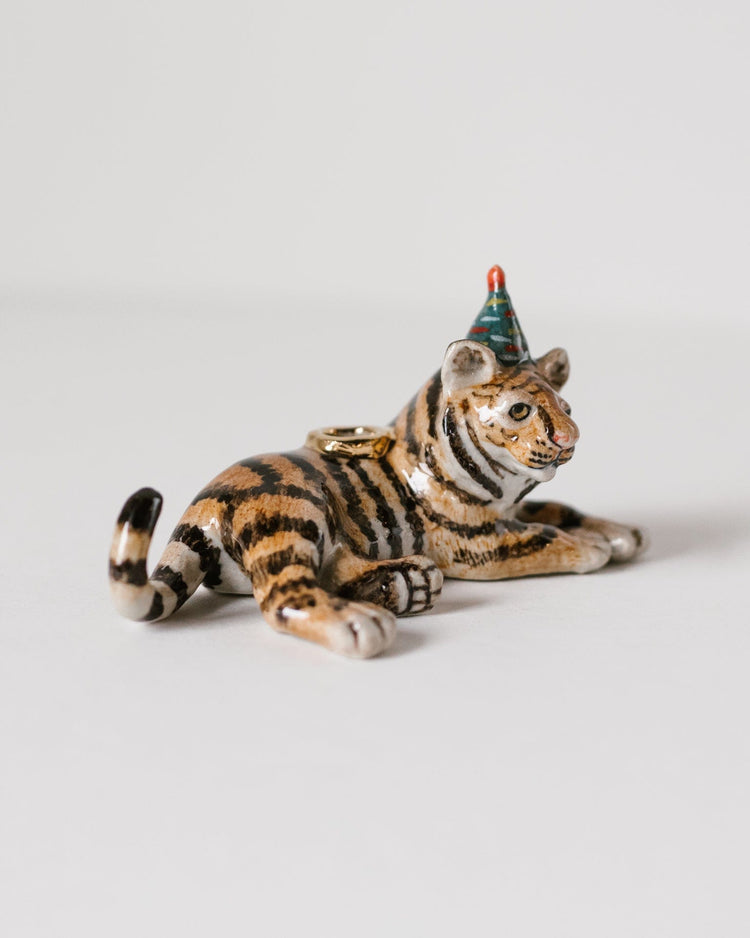 A ceramic figurine of a Camp Hollow Year of the Tiger cake topper wearing a party hat, lying down on a white background.
