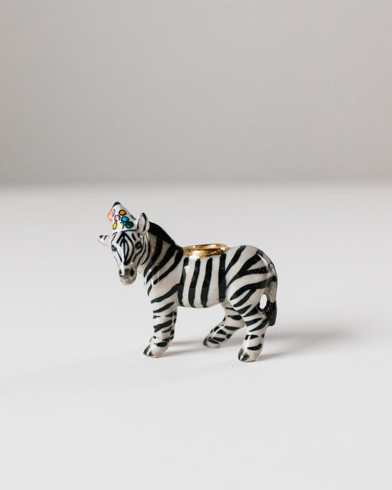 A hand-painted ceramic camp hollow zebra cake topper with a ring holder feature on its back, standing against a plain white background.