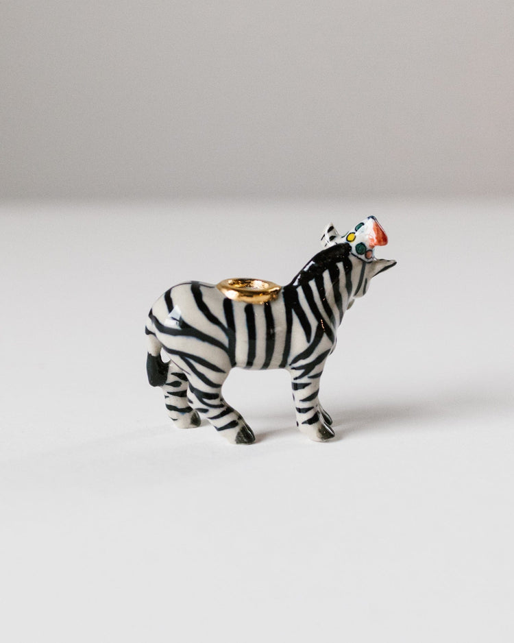A ceramic camp hollow zebra cake topper with a gold ring on its back, photographed against a plain white background.