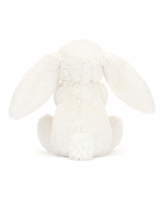 The bashful carrot bunny little by Jellycat is a seated plush toy bunny seen from behind, featuring long floppy ears hanging down its sides and a fluffy tail, all in white. This stuffed animal bunny clutches a tiny carrot.