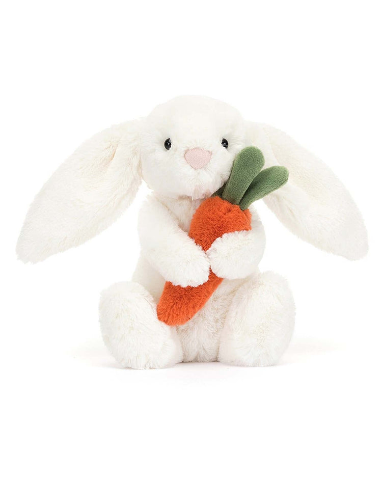 The bashful carrot bunny little by jellycat is a white stuffed animal holding an orange carrot toy with green leaves.
