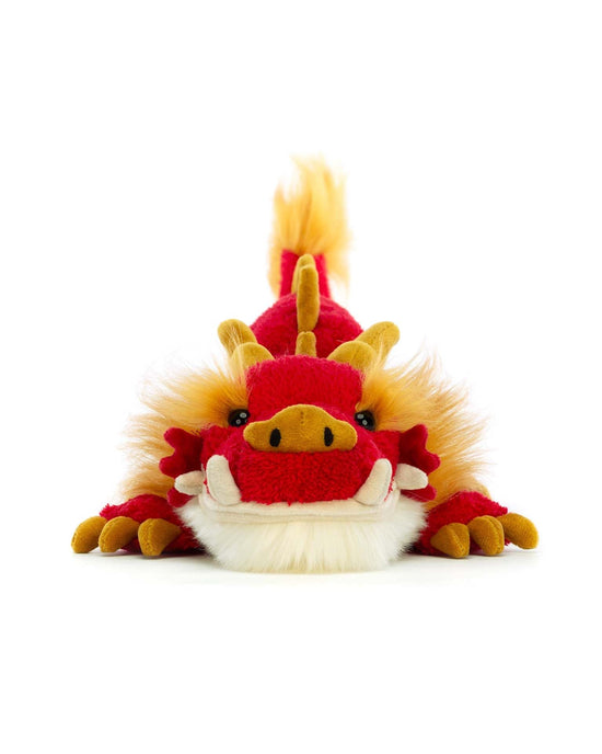 A Jellycat Festival Dragon with yellow accents and a fluffy mane, lying flat on a white background. Perfect for any celebration, this delightful stuffed animal brings a festive touch to any space.