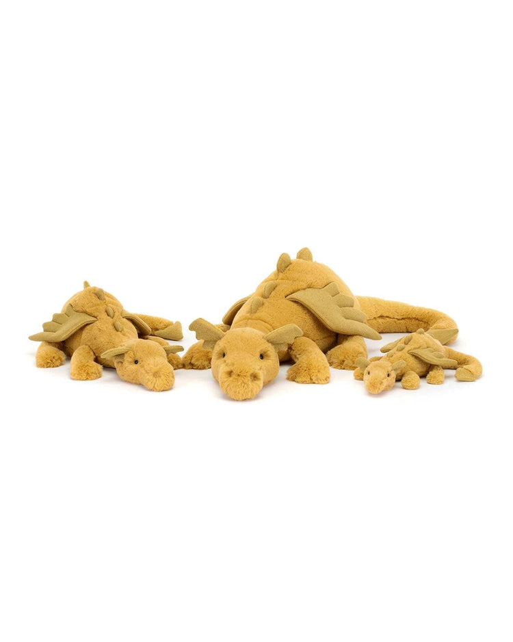 Four golden, soft toy dragons of varying sizes from Jellycat are lying down in a row, facing forward like guardians of magical dreams.