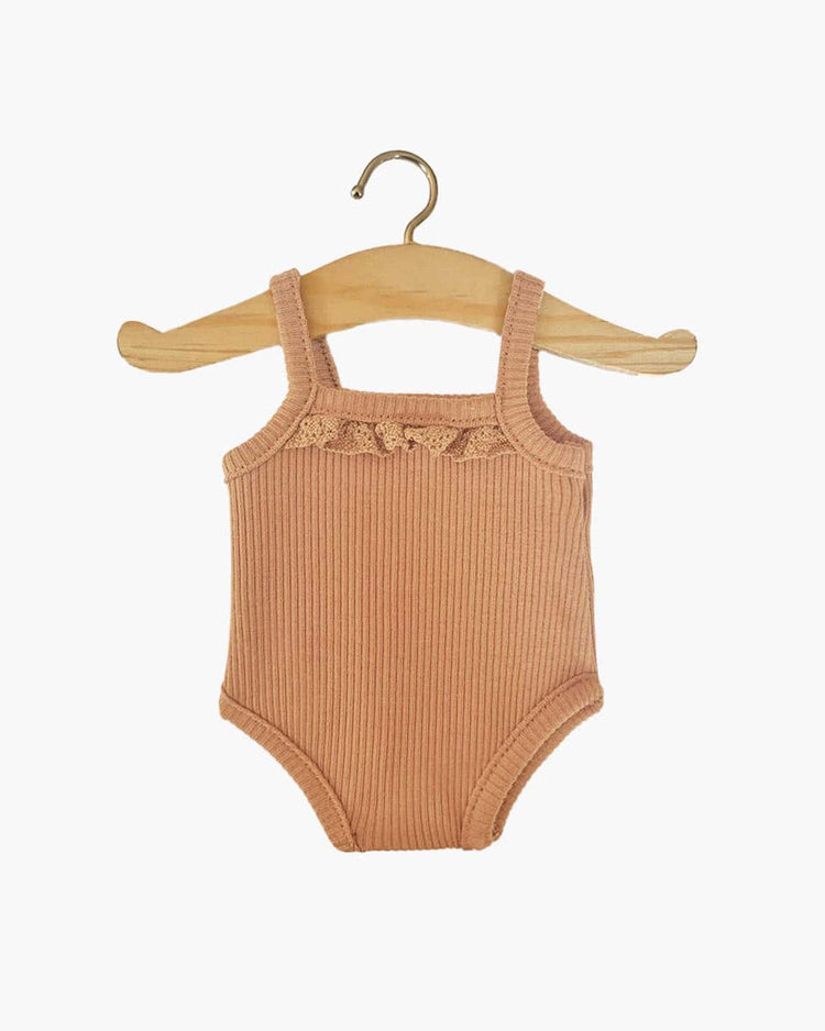 A sleeveless, ribbed baby bodysuit in brown sugar with small lace details on the chest, reminiscent of the delicate outfits designed for timeless dolls like Paola Reina, hanging on a wooden hanger. This charming piece, known as the Les P’tits Basiques ribbed bodysuit by minikane, captures an essence of classic elegance.