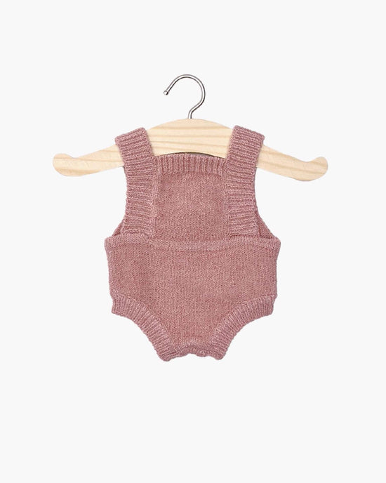 Tea pink lou knit romper featuring shoulder straps, showcased on a wooden hanger against a white background. Perfectly suited for Minikane dolls, it adds a touch of charm to any collection.