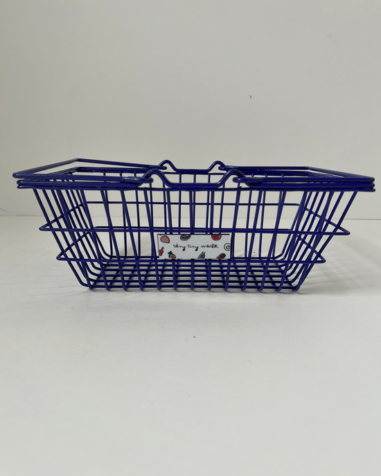 A purple wire basket with a decorative teeny tiny market label on the side stands gracefully on a white surface.