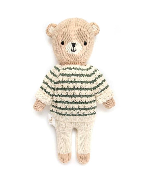 A knitted teddy bear from tun tun, made with Peruvian Pima cotton, is dressed in a natural and green striped sweater paired with cream pants.