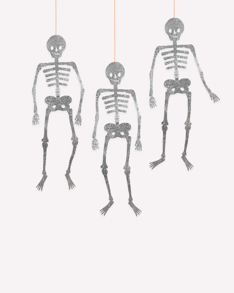 Three giant glitter jointed skeleton decorations by meri meri hang from orange strings against a plain white background, making them perfect as festive Halloween party decor.