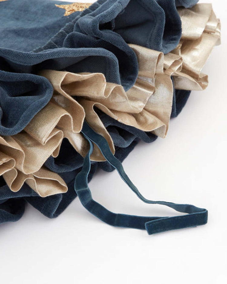 Close-up of layered navy blue and gold ruffled fabric with a matching navy blue drawstring ribbon resting on top, from the meri meri pointed blue hat—perfect as a Halloween accessory or as an elegant trim for a witch hat.