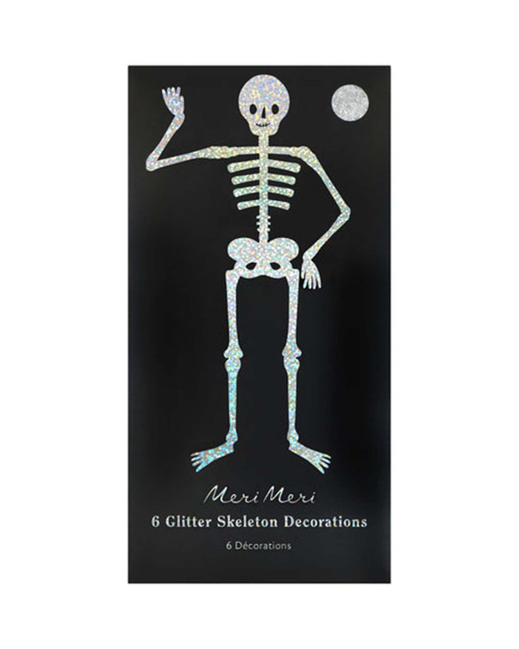 A glittery skeleton illustration waves on a black background beneath a sparkling moon, capturing the playful spirit of Halloween. Text below reads: meri meri glitter jointed skeleton decorations 6 décorations.