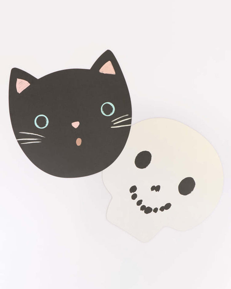 Add a playful touch to your Halloween party tableware with the “halloween heads placemats” from meri meri, featuring stylized cartoon designs of a black cat face and a white skull side by side on a light background.