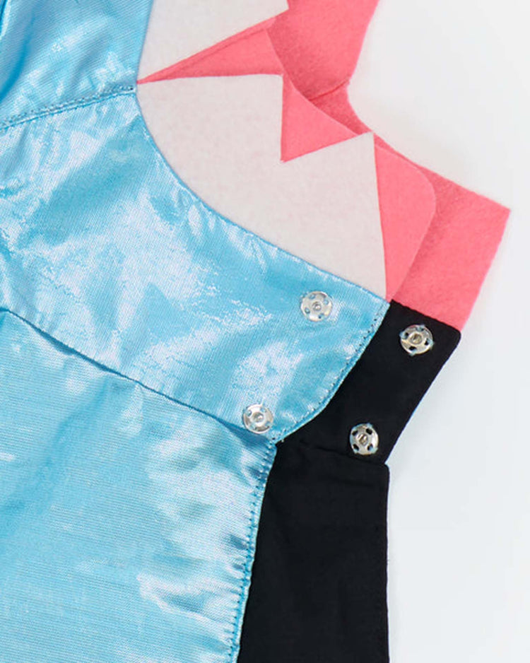 A close-up of shiny blue fabric with metal snaps, pink felt with zigzag edges, and black fabric, all layered together against a white background—perfect details from the meri meri shark costume for inspiring creative or playful sea creature looks.